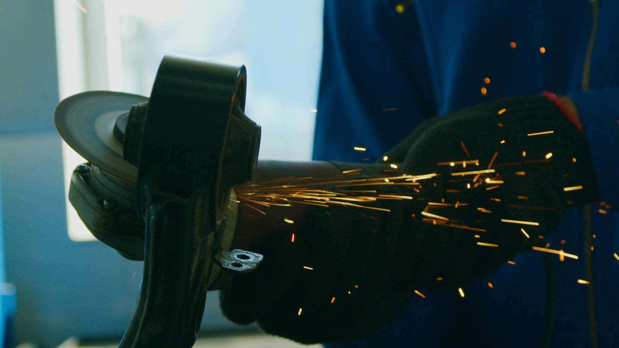 Close-up of a worker using a grinder with sparks flying, showcasing industrial work.