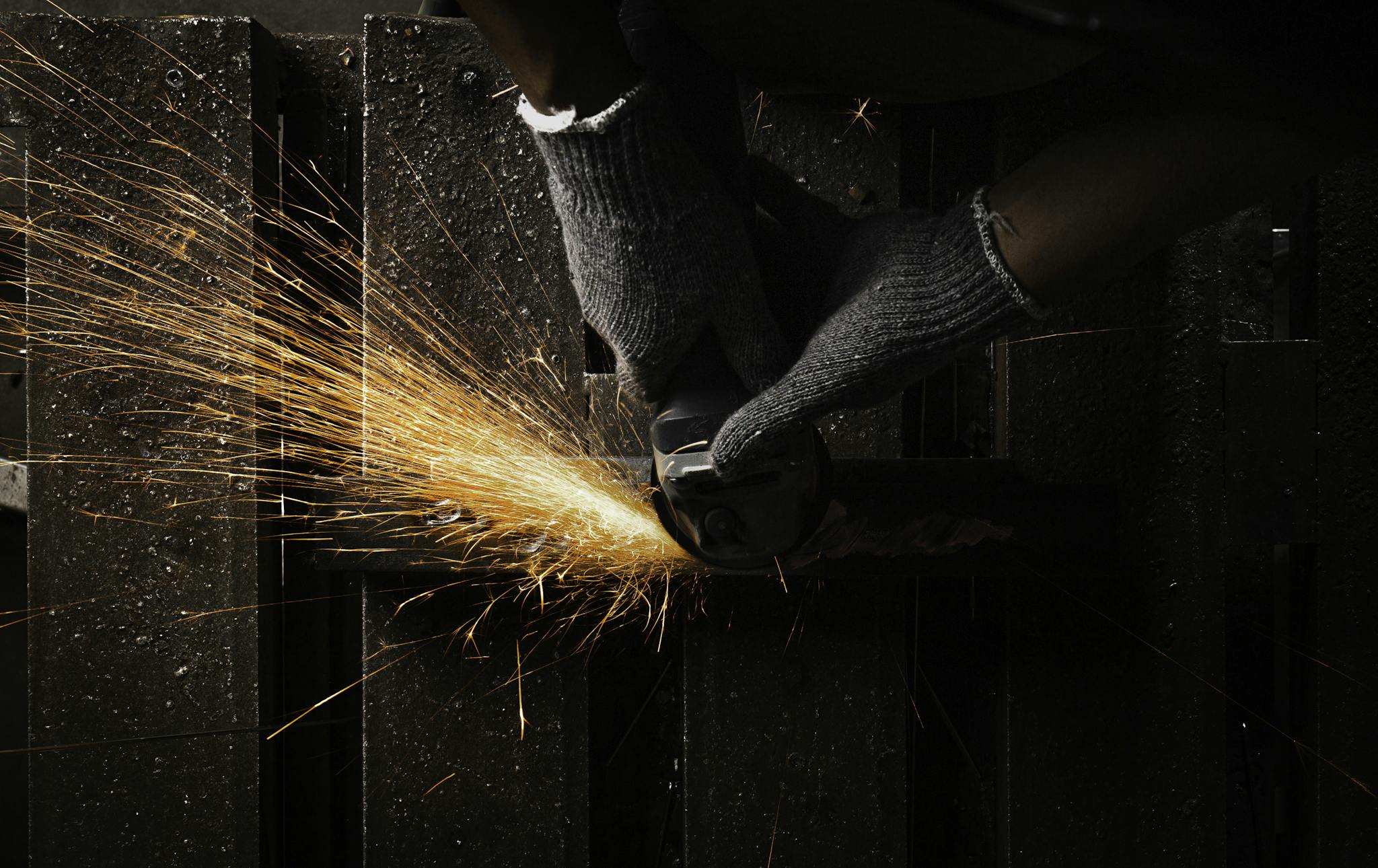 Close-up of an industrial worker using an angle grinder with sparks flying, showcasing metalworking in action.